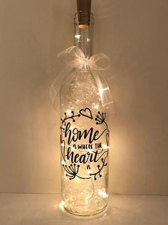 a bottle with some lights in it on a white table and the words home is where the heart is