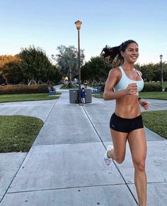 a woman running down a sidewalk in a white bra top and black shorts with her hair blowing back