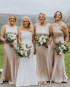 four bridesmaids pose for a photo in their wedding gowns and bouquets