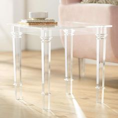 a small clear table sitting on top of a wooden floor next to a pink chair