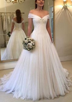 a woman standing in front of a mirror wearing a wedding dress with off the shoulder sleeves