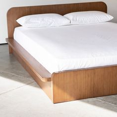 a bed with white pillows and wooden headboard on concrete floor next to wall in room