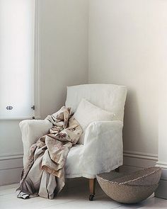 a white chair sitting in front of a window next to a basket on the floor