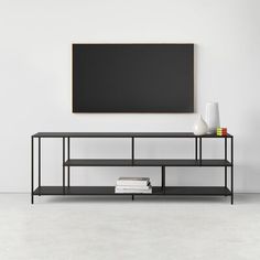 a black shelf with books and vases on it in front of a white wall