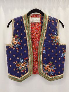 70s Suttles and Seawinds floral vest, royal blue and red floral quilted vest, festival wear look, boho hippie woodstock maximalist style Embrace the bohemian spirit with this vintage 70s Suttles and Seawinds floral vest. A true relic of the Woodstock era, this royal blue and red floral quilted vest exudes festival wear chic and boho hippie maximalism. Made in the charming town of New Germany, Nova Scotia, Canada, this vest is a testament to the craftsmanship and timeless style of Suttles and Seawinds. The vibrant royal blue base is adorned with lush red floral patterns, creating a striking contrast that captures the essence of 70s fashion. The quilted design not only adds a layer of warmth and texture but also speaks to the artisanal quality of this piece. Perfect for layering, this vest w Bohemian Floral Print Spring Vest, Blue Sleeveless Vest For Festival, Bohemian Floral Print Summer Vest, Blue Cotton Festival Vest, Retro Blue Vest For Spring, Red Vest For Fall Festival, Fitted Blue Vest For Festival, Bohemian Fitted Vest For Festival, Fitted Bohemian Vest For Festivals