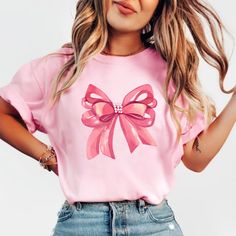 Embrace elegance and flirtatious charm with our captivating pink bow shirt, a delightful addition to your coquette-inspired wardrobe! 🌸👚 This shirt embodies the essence of femininity and playfulness, perfect for those who adore a touch of chic sophistication with a hint of flirtation. 🌷 The darling pink hue complements the shirt's design, accentuating the focal point--an exquisitely crafted oversized bow adorning the neckline or sleeves, adding a whimsical and flirtatious allure to your ensem Pink Party Top With Bow, Pink Tops With Bow For Party, Feminine Party Tops With Bow Detail, Cute Pink T-shirt With Bow, Cute Party Tops With Bow, Cute Party Tops With Bow Detail, Feminine Tops With Ribbon For Spring, Feminine Ribbon Tops For Spring, Cute Bow T-shirt For Spring