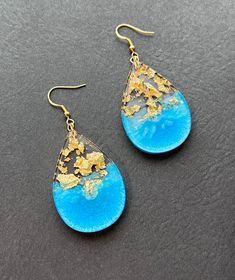 two pairs of blue and gold earrings on a black surface, with one pair dangling from the