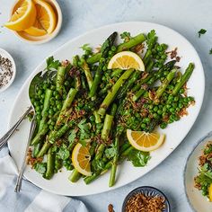 asparagus and lemons on a white plate with silver spoons next to it