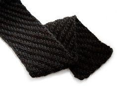 a black knitted scarf laying on top of a white surface