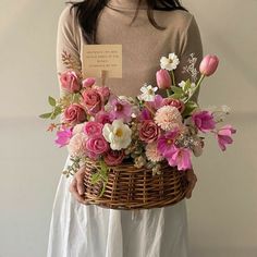 a woman holding a basket with flowers in it and a note attached to the handle