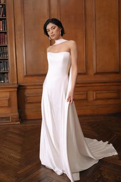 a woman in a white dress standing on a wooden floor with bookshelves behind her