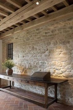 a room with stone walls and brick flooring is shown in the foreground, along with a wooden bench that has a potted plant on it's side