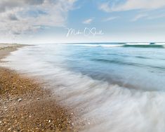 there is a beach with waves coming in to the shore and blue sky above it