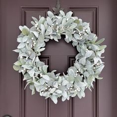 a wreath is hanging on the front door, with white flowers and green leaves around it