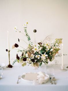 a white table topped with a vase filled with flowers next to two candles and plates