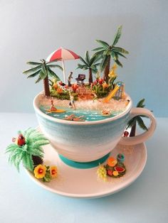 a tea cup with a miniature beach scene in the top and bottom, sitting on a saucer