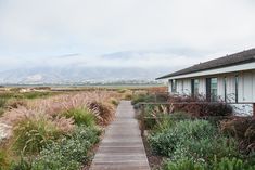 a wooden walkway leading to a house with mountains in the background