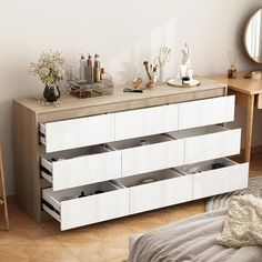 a white dresser with drawers in a bedroom next to a mirror and table on the floor