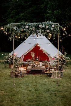 a tent set up in the middle of a field with flowers and candles on it