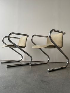 two chairs sitting next to each other on top of a cement floor in front of a white wall