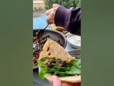 a hand holding a sandwich with meat and lettuce on it, in front of other dishes