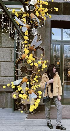 a woman standing in front of a building with yellow flowers on the side of it