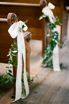 two wooden pews decorated with white ribbons and greenery