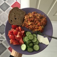 a purple plate topped with sliced cucumbers, bread and tomatoes next to a fork