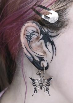 a close up of a person's ear with tattoos on it and a butterfly dangling from the side