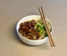 a white bowl filled with meat and vegetables next to chopsticks