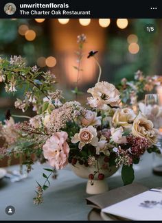 an arrangement of flowers in a vase on a table with candles and lights behind it