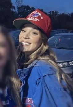 a woman wearing a red hat and blue jacket standing in front of a parked car