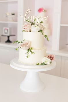 a white wedding cake with flowers on top and the word love spelled in cursive letters