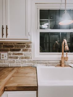 a kitchen sink sitting under a window next to a wooden counter top in front of a brick wall