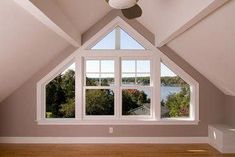 an empty room with a ceiling fan and large windows overlooking the water in the distance