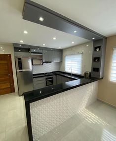 an empty kitchen with black counter tops and stainless steel appliances in the center, along with white tile flooring