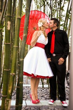 a man and woman kissing in front of bamboo trees with red umbrellas on their heads