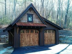 two garages with wooden doors in front of a stone wall and trees behind them