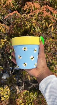 a hand holding a blue cup with bees on it and a green plastic stopper