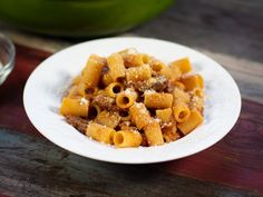 a white plate filled with pasta and sauce on top of a wooden table next to a glass of water