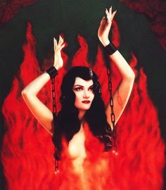 a woman with chains around her neck and hands in the air, surrounded by flames