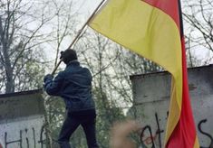 a man holding a yellow and red flag in front of some graffiti on a wall