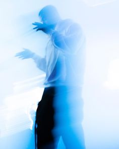 a blurry image of a man in white shirt and black pants standing next to a wall