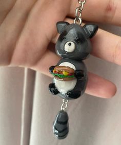 a hand holding a black and white bear keychain with a hamburger in it