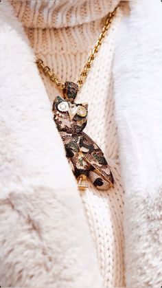 a person wearing a white sweater and a gold necklace with an owl pendant on it