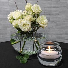 a glass vase filled with white roses and a lit candle on top of a table