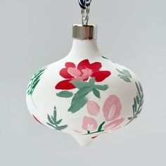 a white ornament with red and green flowers on it's side hanging from a chain