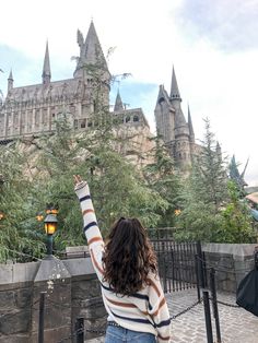 a woman standing in front of hogwarts castle waving to the sky with her hand up