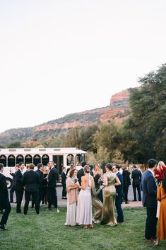 a group of people standing on top of a lush green field next to a white bus