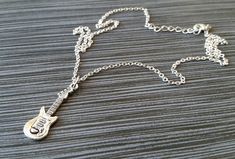 "Personalized Silver Guitar Necklace! A detailed three dimensional electric guitar charm on a bright silver chain makes the perfect gift for you or your favorite musician. The guitar charm is made from zinc alloy and measures 30 mm by 10 mm. The chain is silver plated and measures 16\" or 18\" with a 1\" extender. You can also personalize your necklace with a .5\" silver plated disc stamped with the initial of your choice (see last picture). To order your necklace WITHOUT a custom stamped initia Silver Rock Style Necklace Gift, Silver Rock Style Necklace As Gift, Silver Rock Style Necklace For Gift, Music Necklaces, Guitar Necklace, Silver Trumpet, Silver Guitar, Football Bracelet, Music Necklace